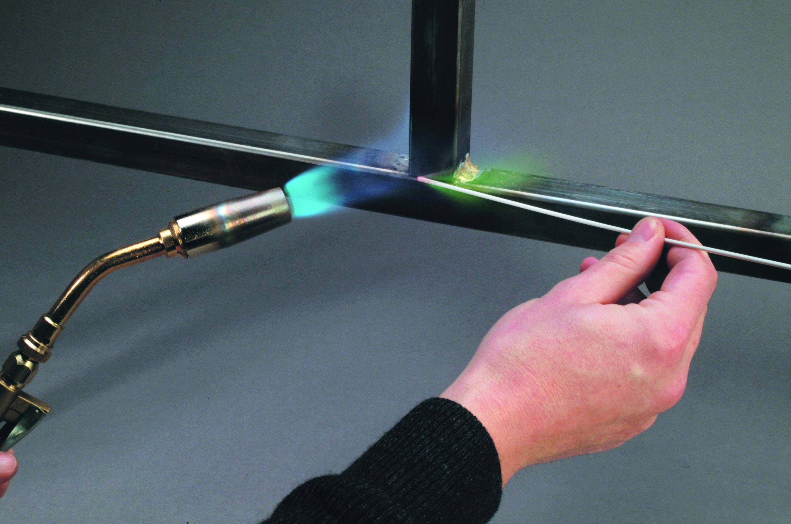 A person is soldering two metal parts together using a flame and a soldering iron.