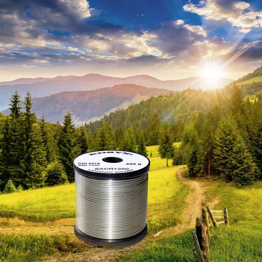 A silver wire reel sits in a picturesque landscape with forests, hills, and a sunset in the background.