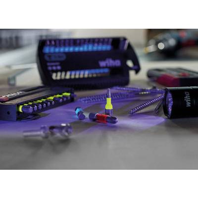 Several screwdriver bits and accessory parts are laid out on a table. Background blur shows tools. The main colours are blue and purple.