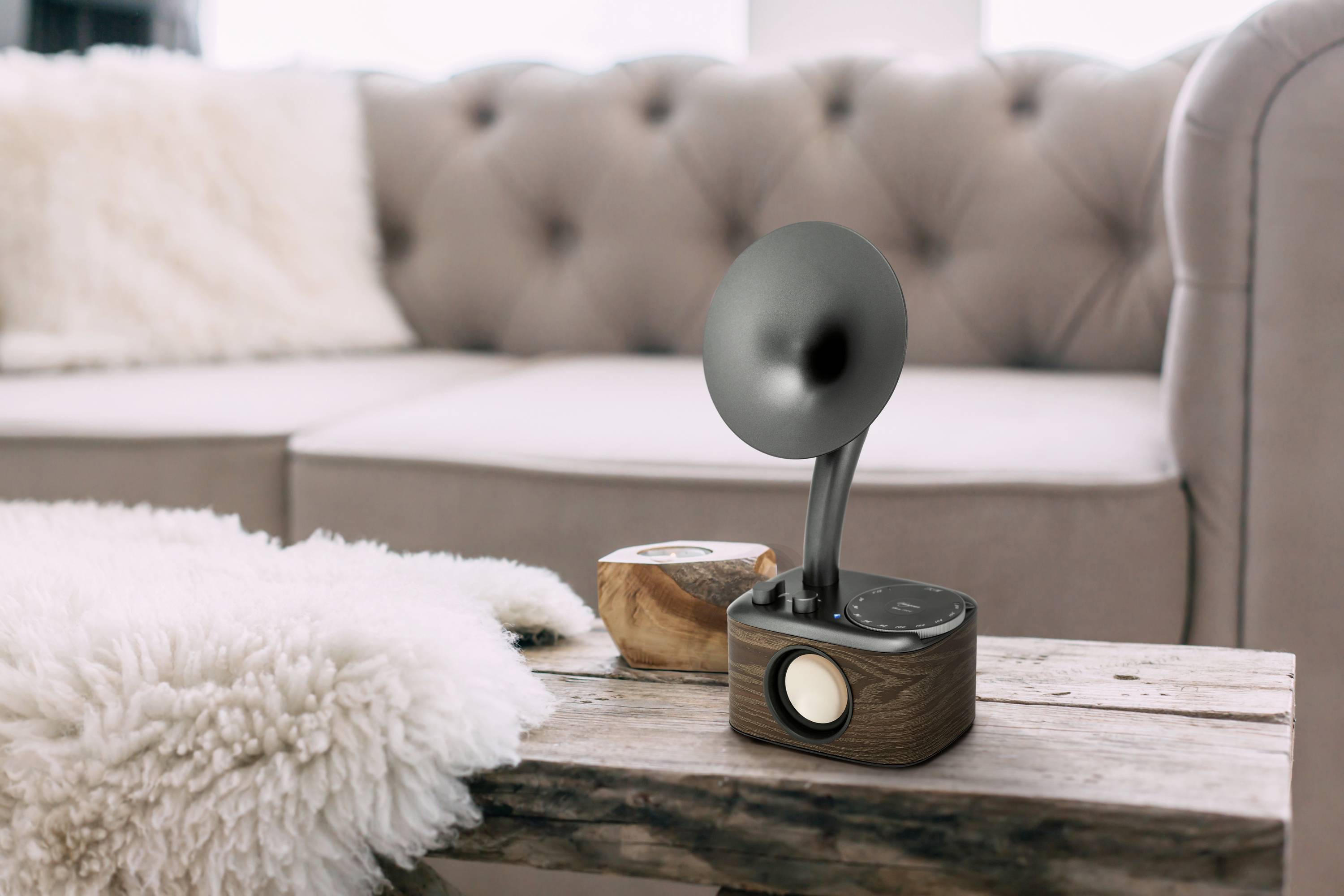 A vintage radio with a wooden casing and a black speaker horn sits on a table in front of a beige sofa with cushions.