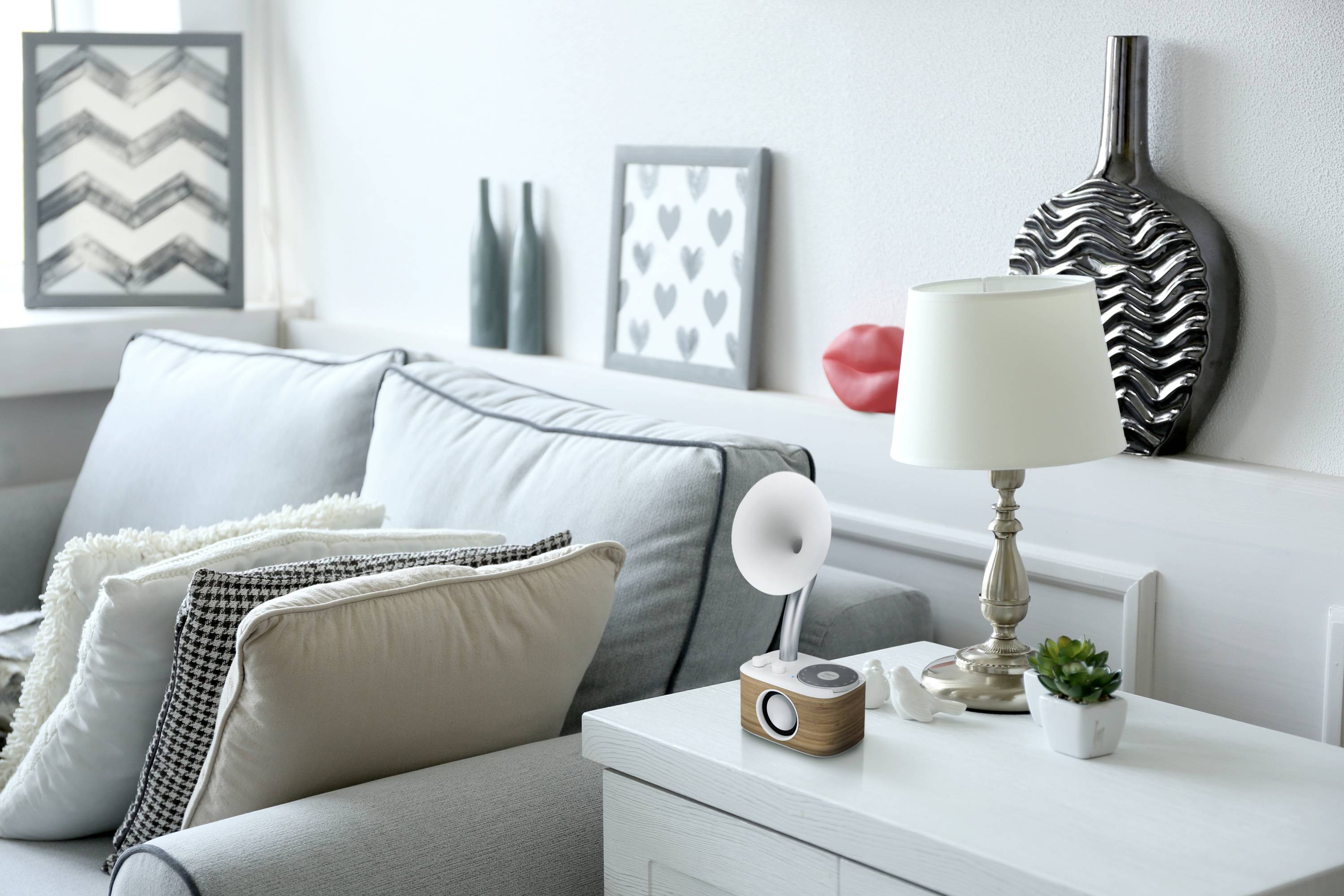 Cosy living room with a light-coloured sofa, decorative cushions, a table lamp, and plants on a side table.