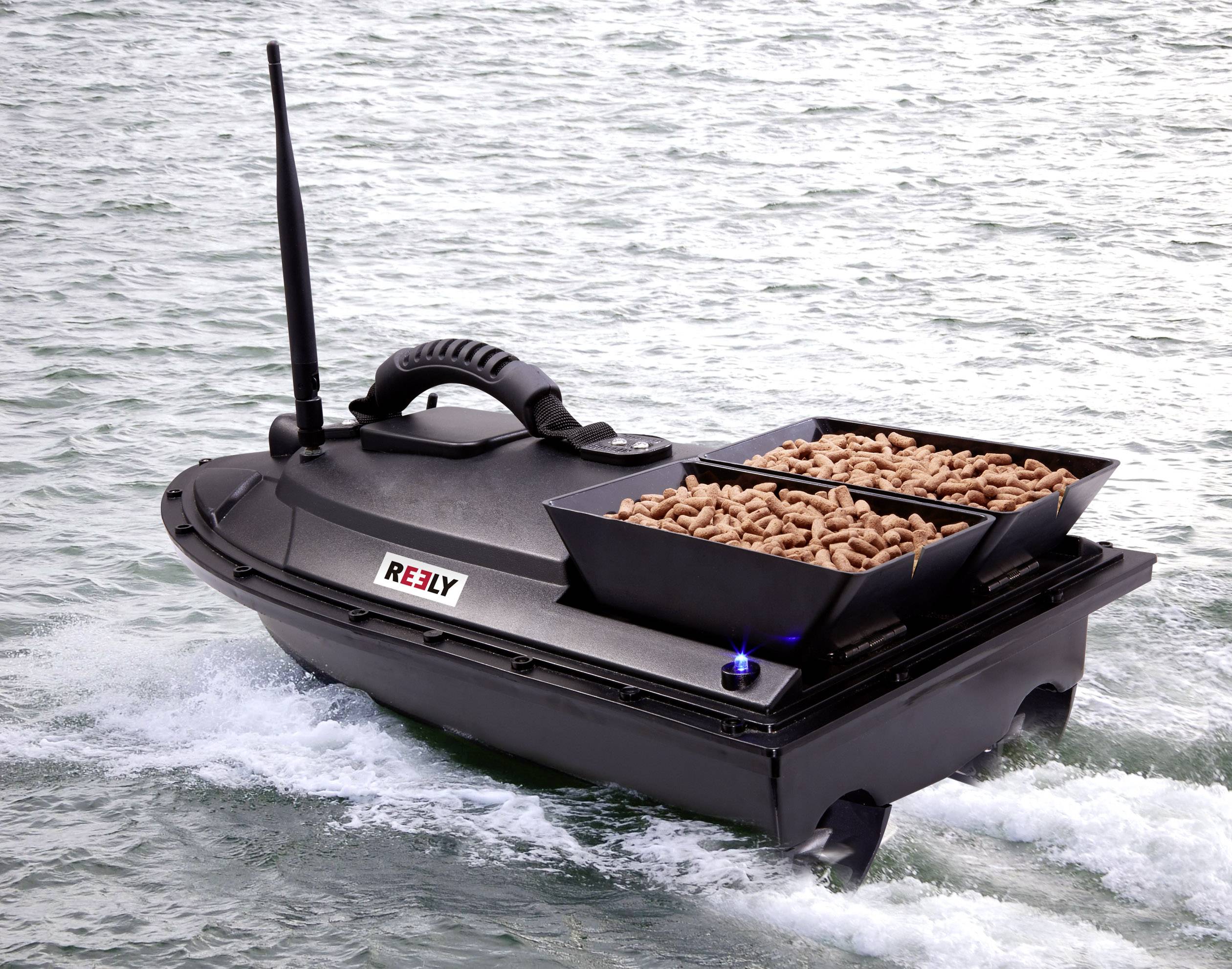 Black remote-controlled boat on water, transporting two containers with pellets and equipped with an antenna mast.