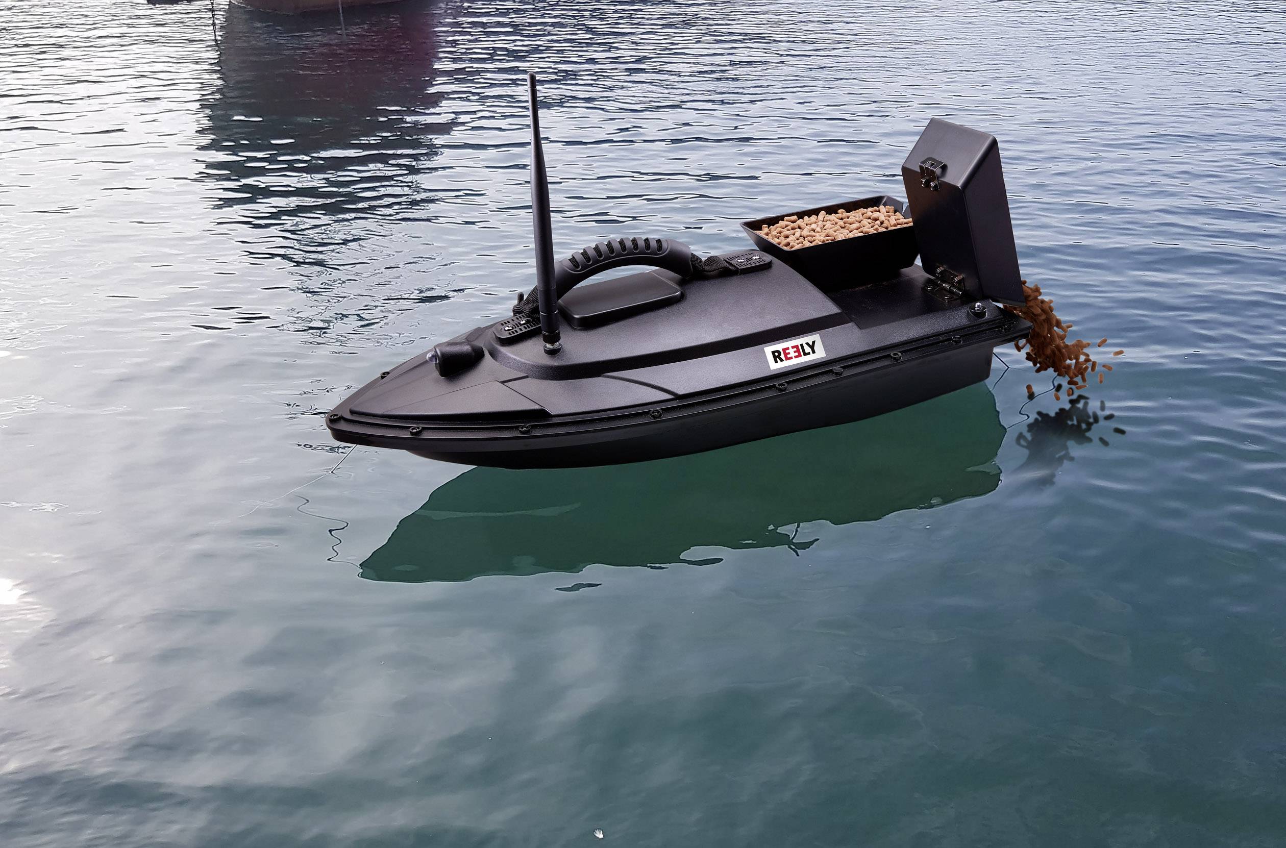 A black remote-controlled boat is on the water, scattering feed into the water.