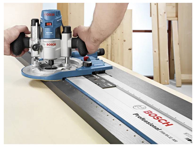 A person is using a Bosch router on a guide rail to cut a wooden board, showcasing precise woodworking equipment.