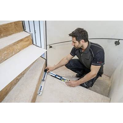 A person measures a staircase using a digital level, possibly for renovations, highlighting precision in construction work.