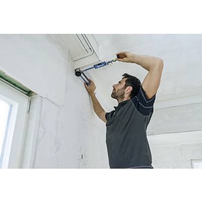 A man is installing an air conditioning unit on a wall inside a room. He is using a tool to secure the unit in place.