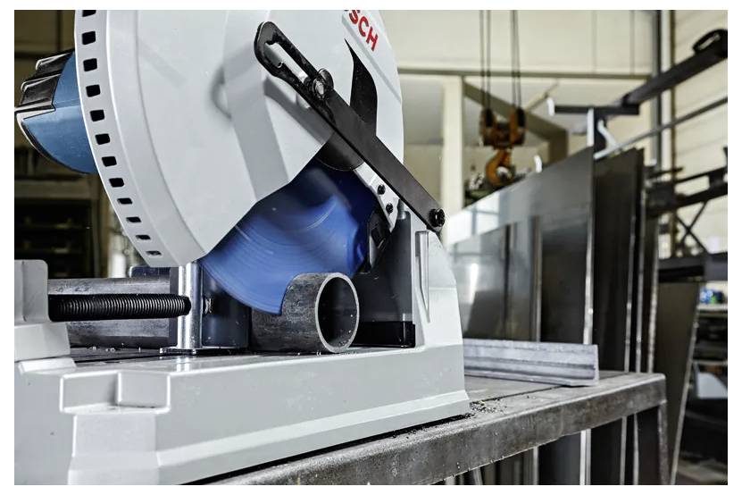 A power tool with a rotating blue blade cuts a metal pipe in an industrial workshop setting.