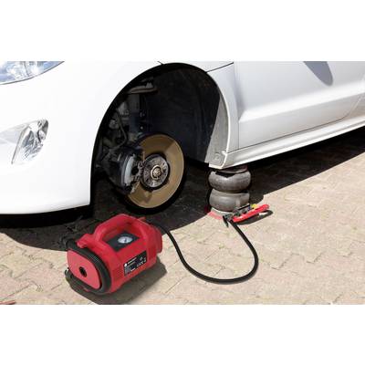 A car is being raised with a pneumatic jack, with no wheel mounted on the front axle. A compressor is positioned next to the car.