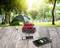 A portable power bank charges two mobile devices on a wooden table in front of a tent in a sunny forest.