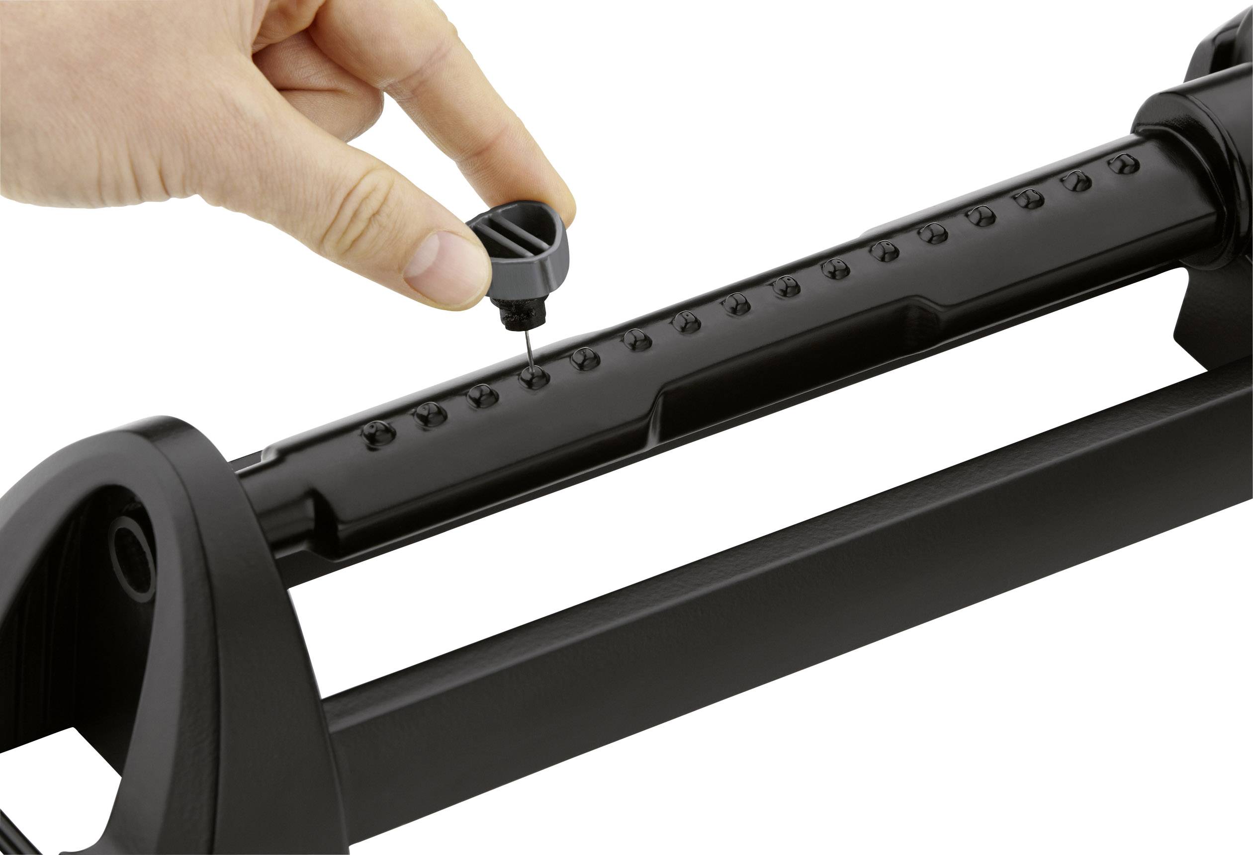 A hand adjusts the spray range of a black lawn sprinkler by moving a small grey cap on the water outlet.