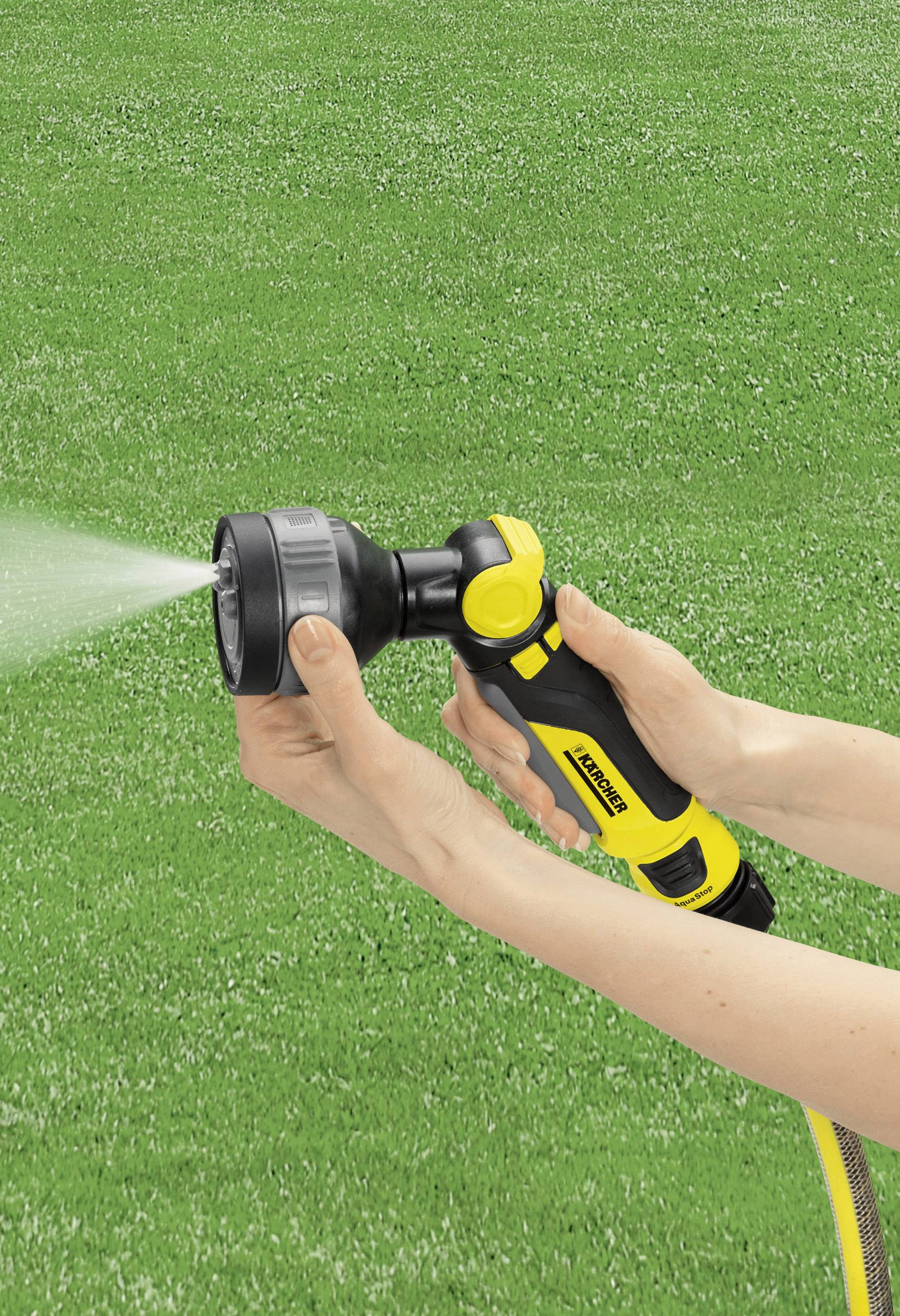 A hand is holding a yellow spray nozzle, spraying water onto a green lawn.