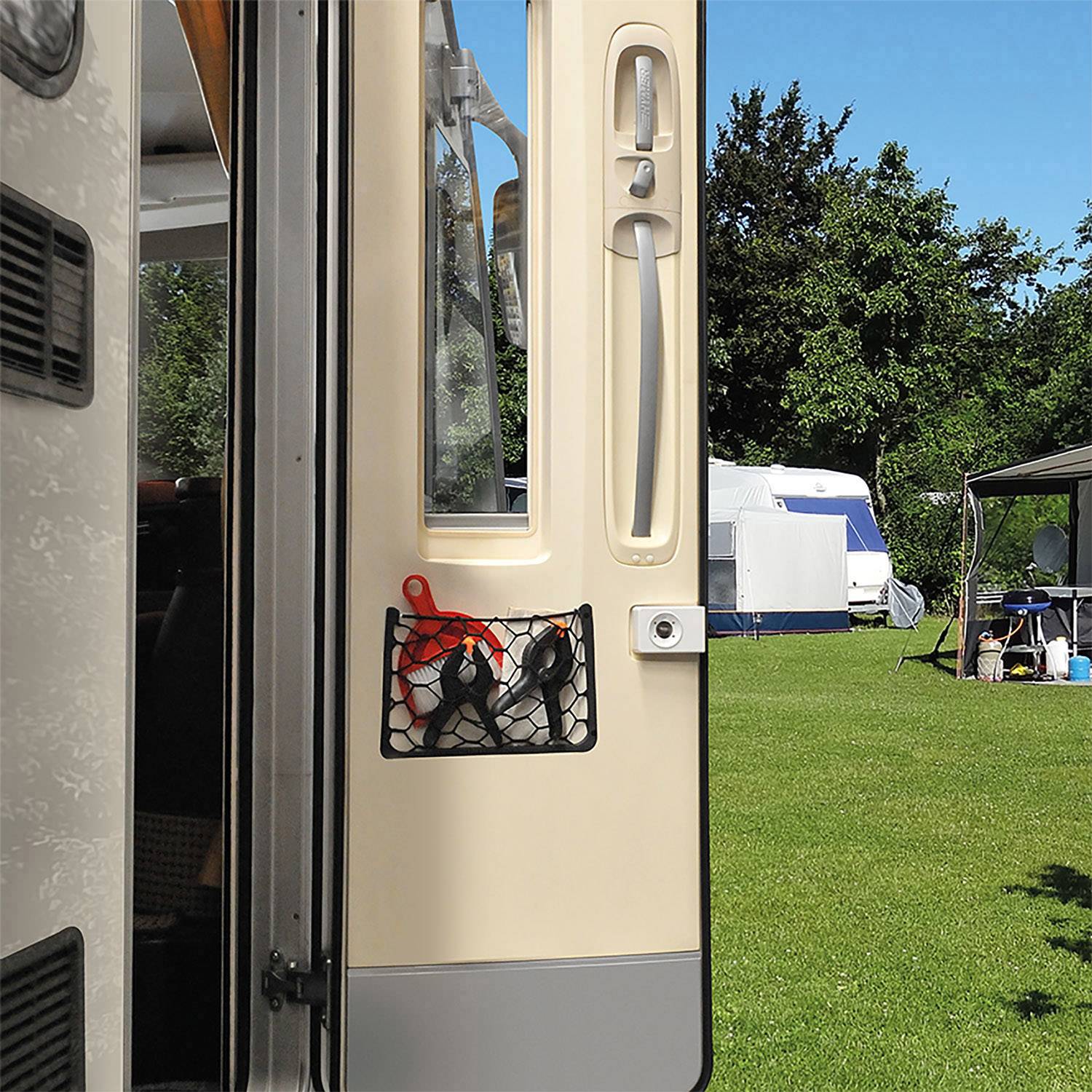 View from a caravan onto a sunny campsite with green grass and trees. In the background, tents and motorhomes are parked.