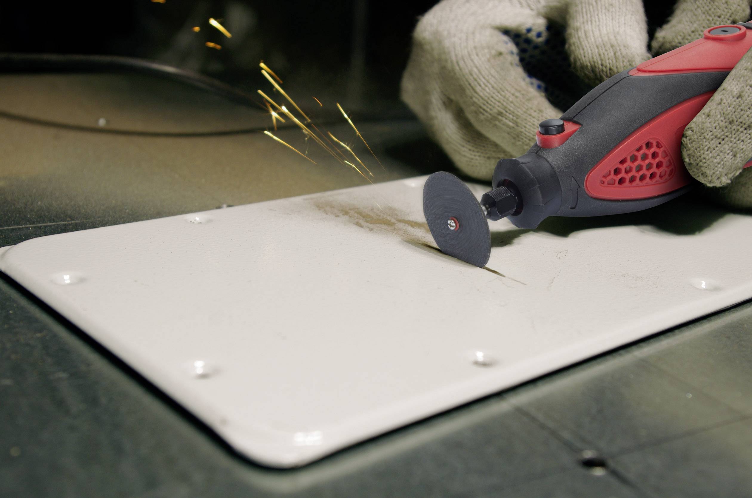 A person is using a red and black handheld tool with a grinding disc to work on metal. Sparks are flying.