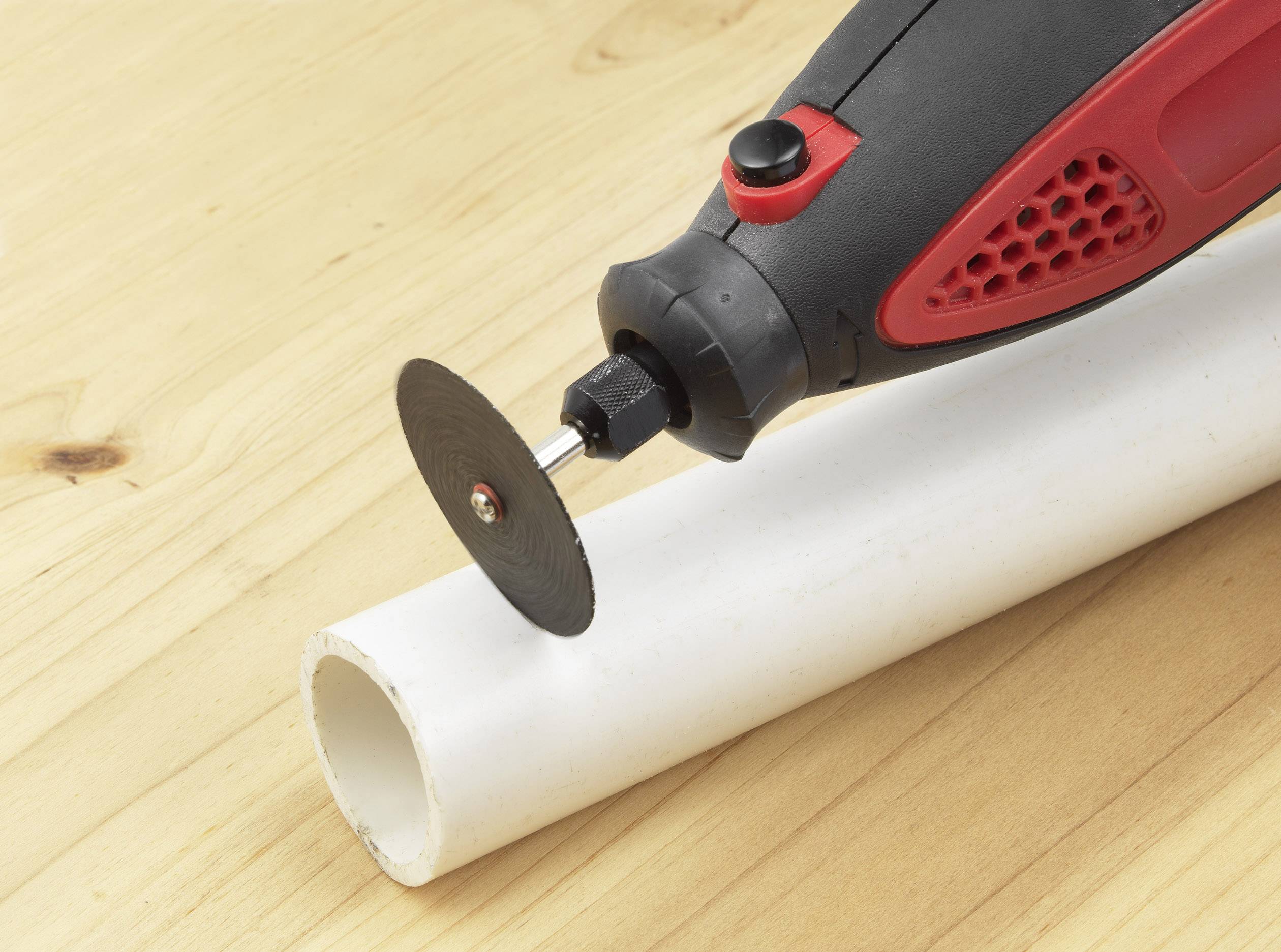 A black and red rotary tool is cutting a white PVC pipe on a wooden table.