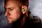 A man with a green earplug looks forward. The background is blurred.