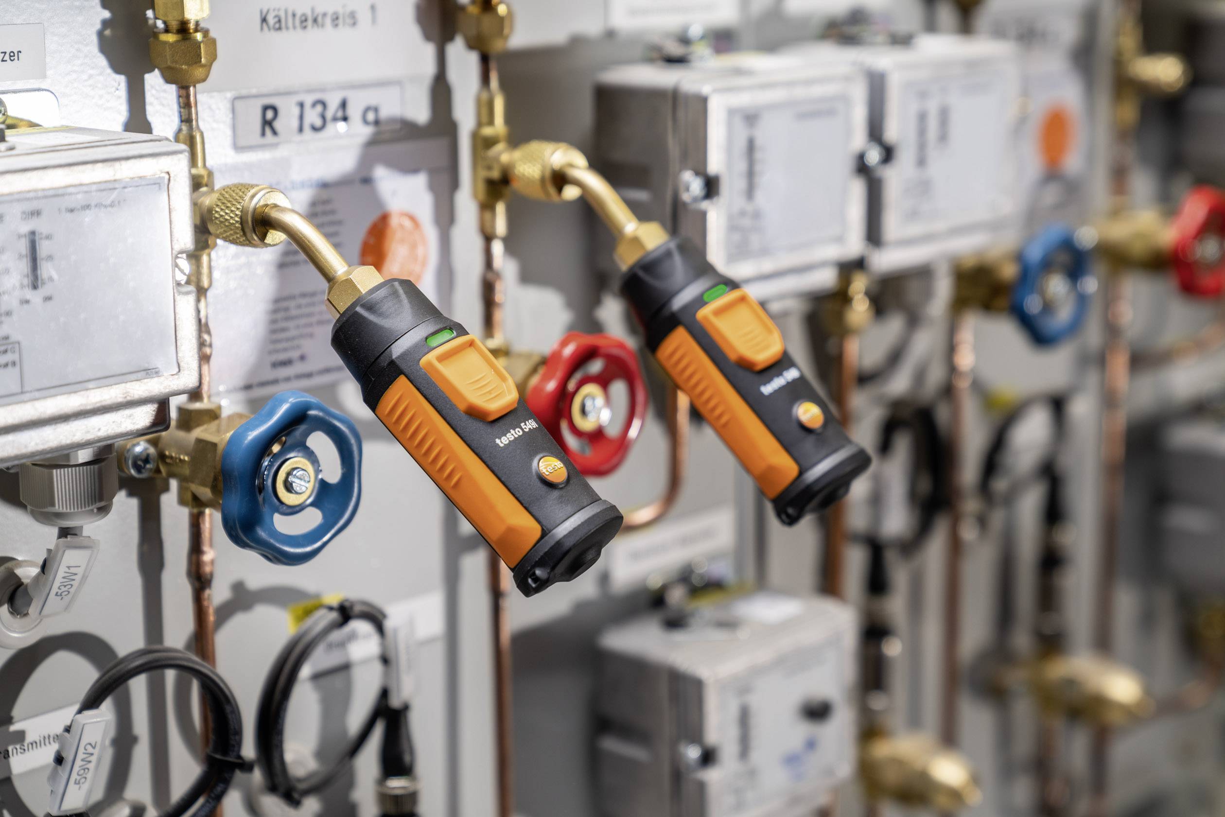 Two orange sensors are mounted on pipes in a technical installation, possibly for measuring or controlling liquids.