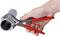 A red pipe wrench grips a metal pipe. A hand holds the wrench, adjusting and opening it.