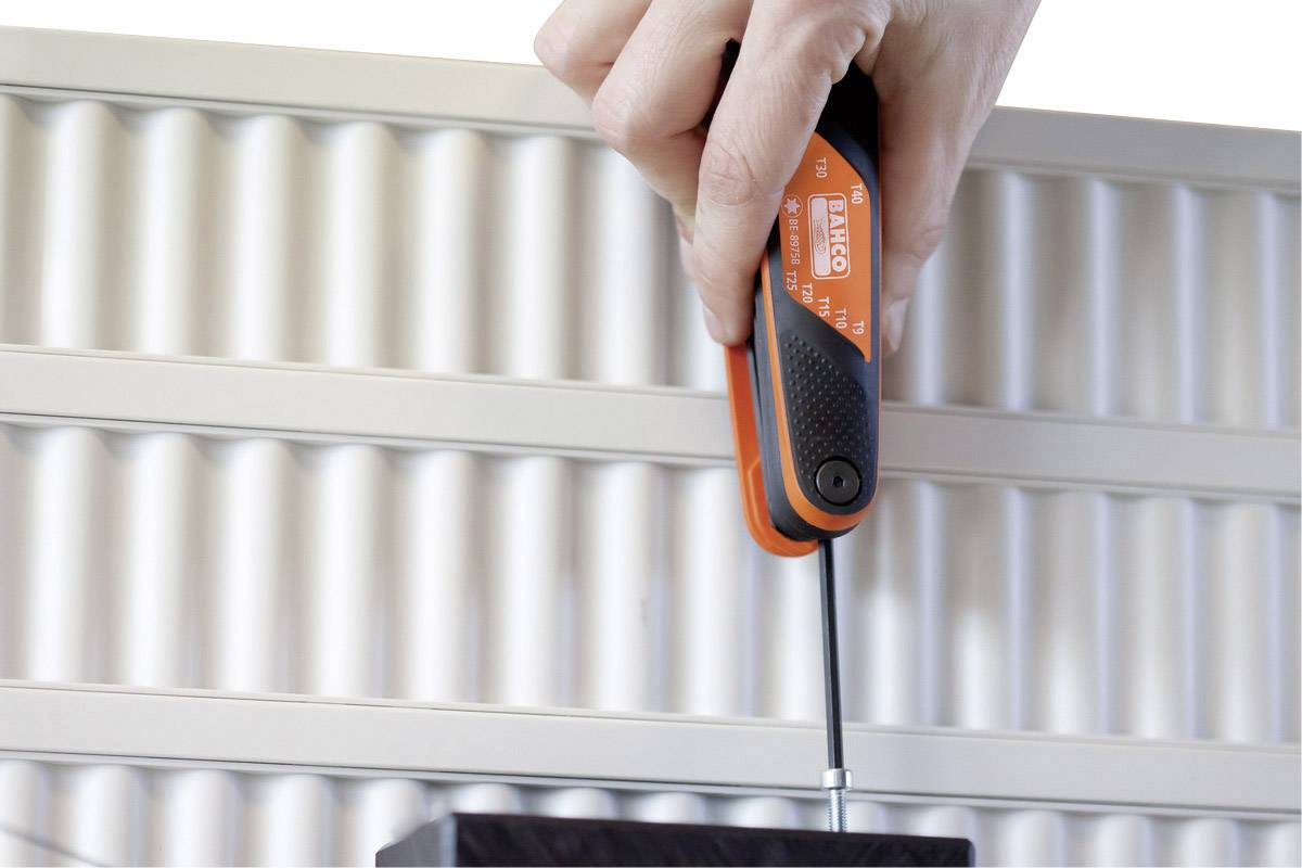 A hand holds a screwdriver and tightens a screw on a wavy metal panel.