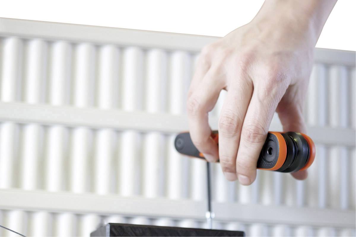 A hand is holding a screwdriver and tightening a screw in the foreground. An abstract wall pattern is visible in the background.