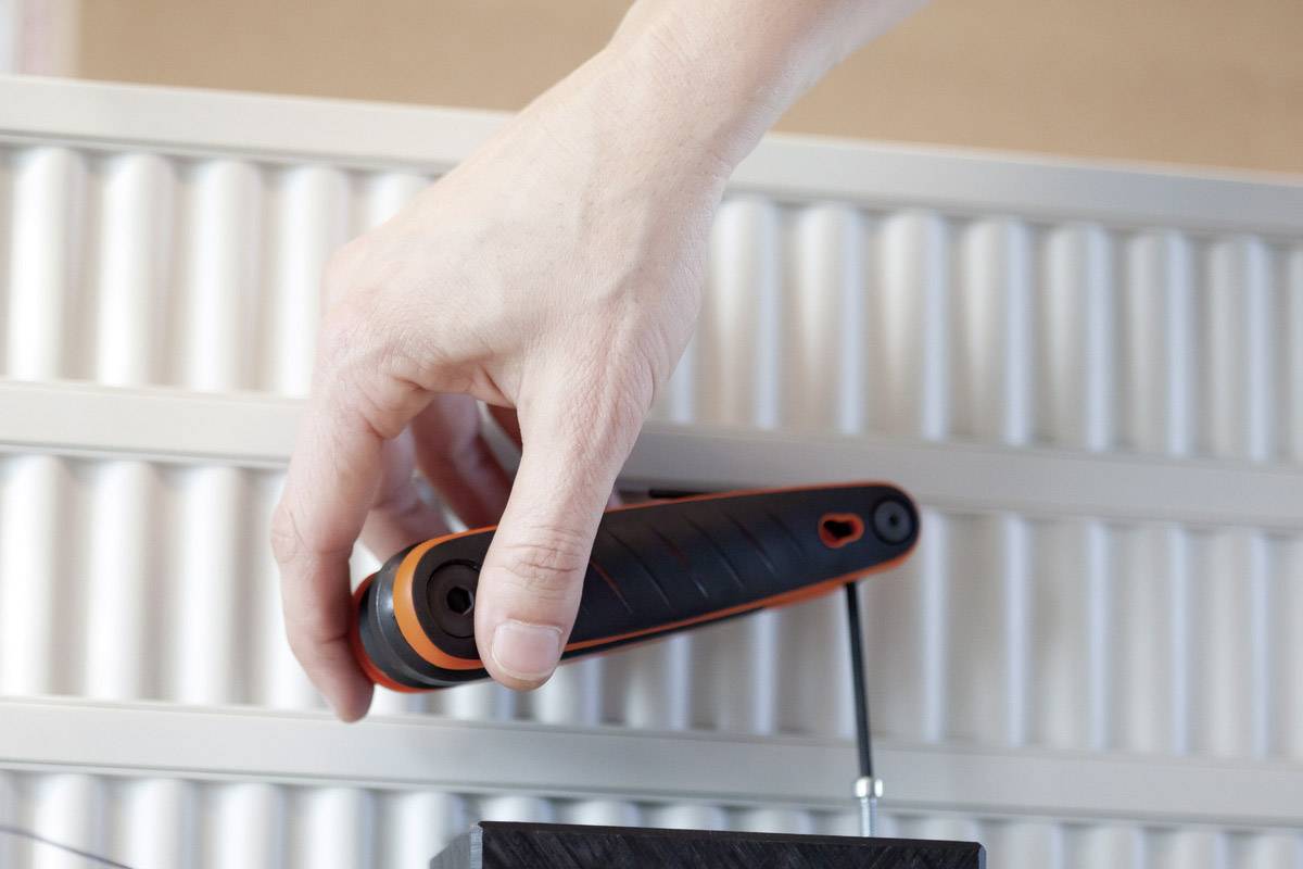 A hand is holding a tool with a black handle and orange border, against a background with a ribbed pattern.