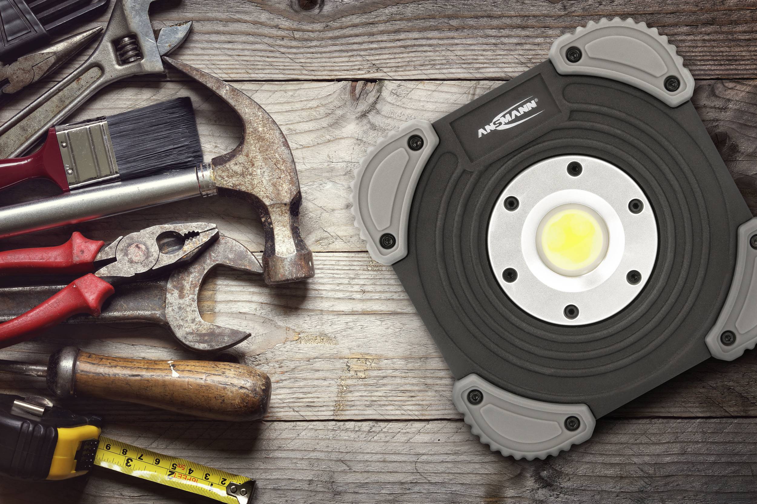 Tools on a wooden surface: hammer, screwdriver, pliers, paintbrush and tape measure. A work light on the right.<br><br>Note: The translation is already in British English, so no significant changes were needed.