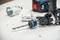 Cordless drill with hole saw attachment inserted. Background shows several saw attachments and a blurred tool.