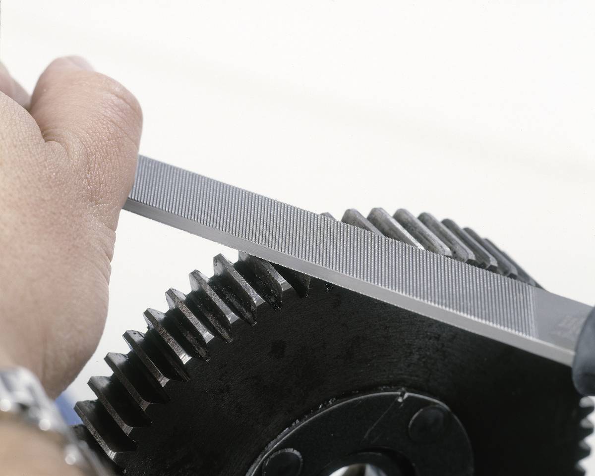 A hand is filing the teeth of a metal gear. Mechanical machining for fine-tuning or repair of the gear.