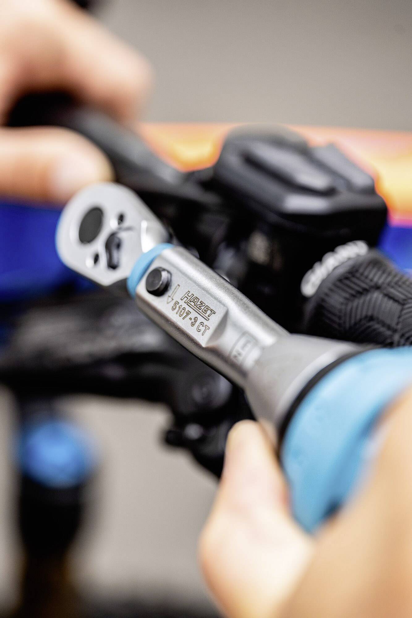 A person is adjusting a screwdriver on a bicycle part. The screwdriver displays an inscription with torque specifications.
