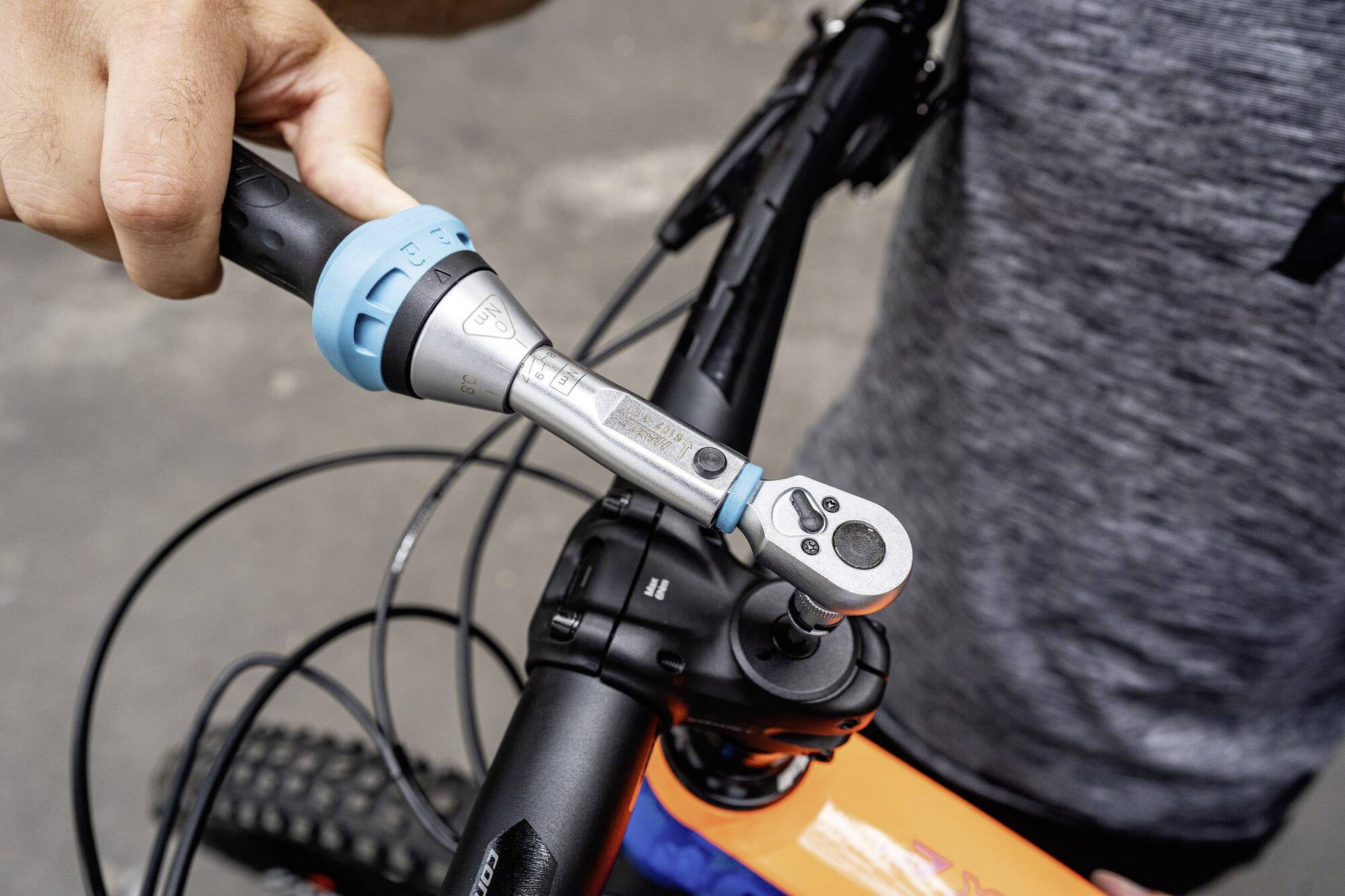 A person is adjusting the handlebars of a bicycle using a torque wrench to secure the bolts.