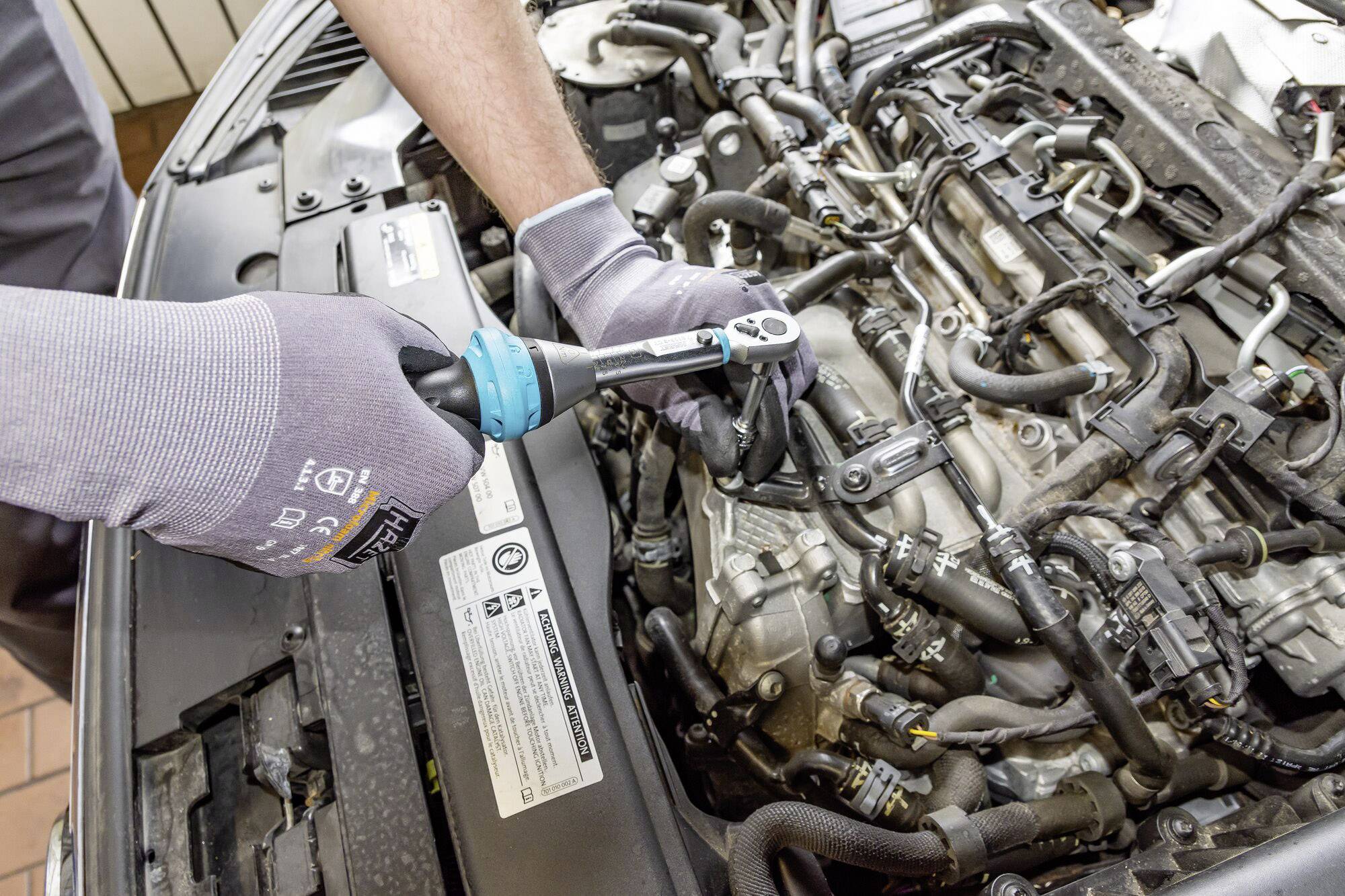 A mechanic is repairing a car engine with a torque wrench positioned on a bolt on the motor. The mechanic is wearing gloves.
