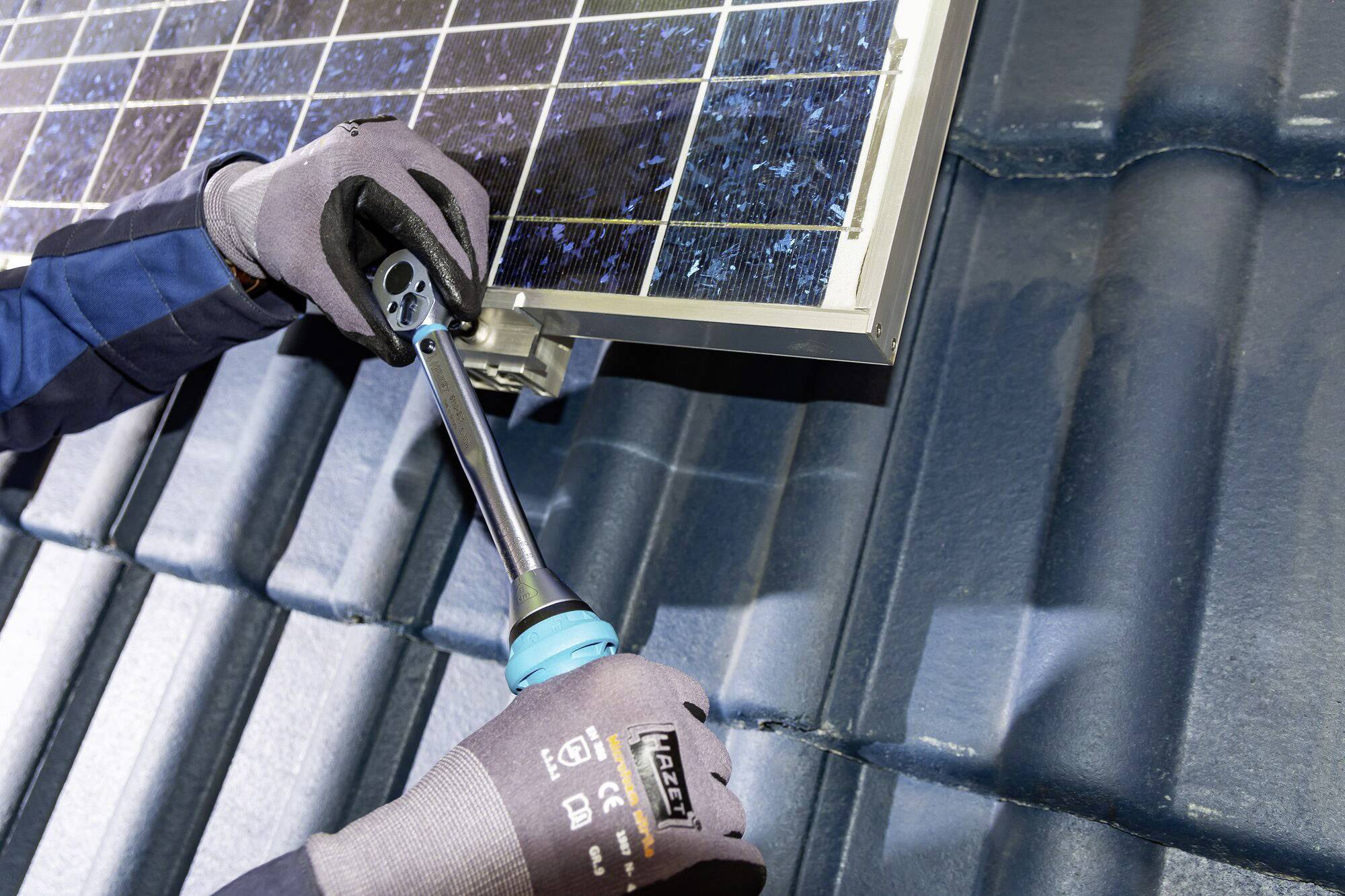 A person is installing a solar panel on a roof. They are wearing gloves and holding a tool, securing the panel to the mounting bracket.