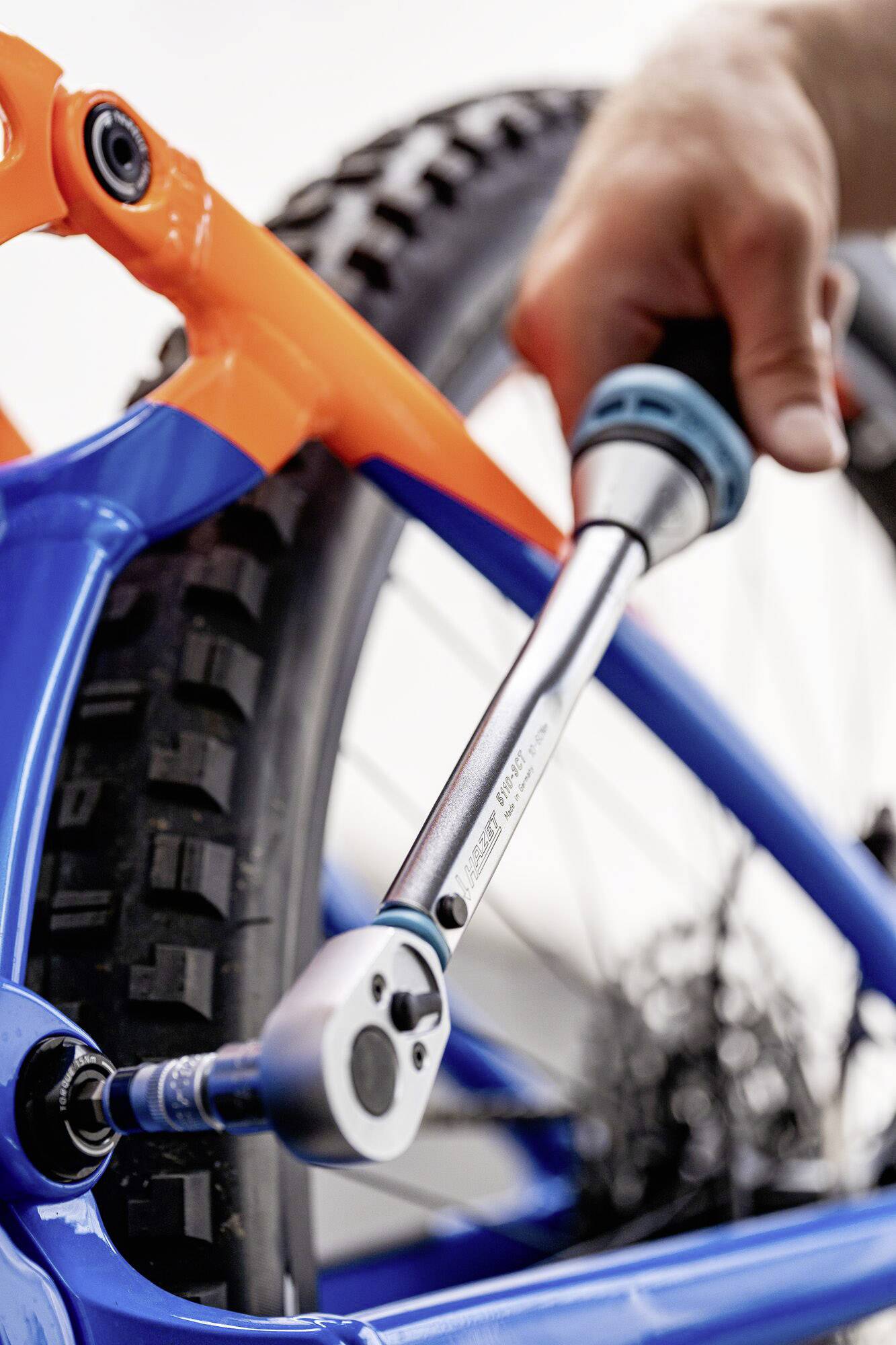 A hand is using a torque wrench to tighten a screw on a blue and orange bicycle tyre.