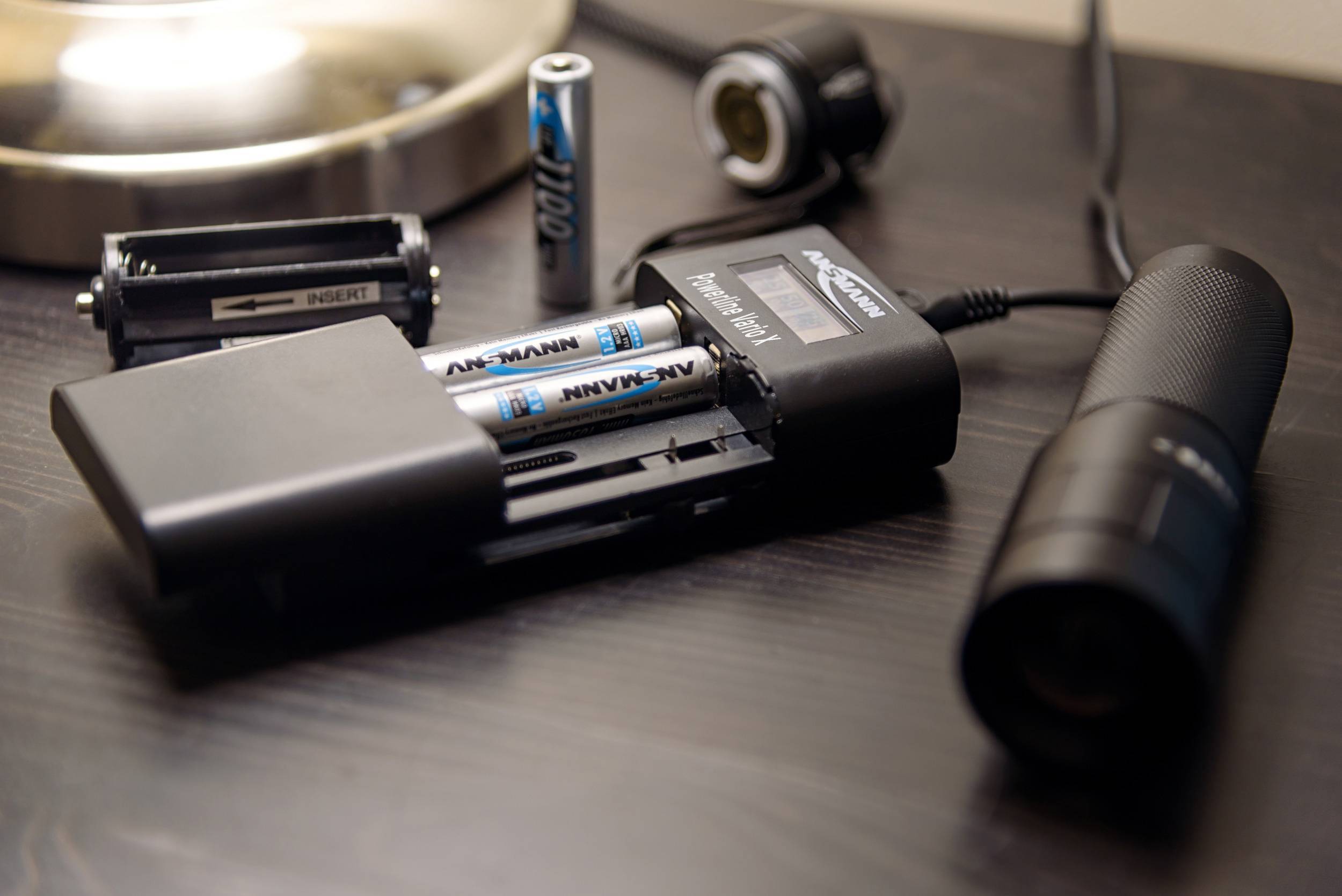 Battery charger on a table charging two AA batteries. Next to it, a torch and additional batteries.