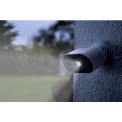 A fixed security camera mounted on a wall focused on a garden at dusk, with lights switched on.