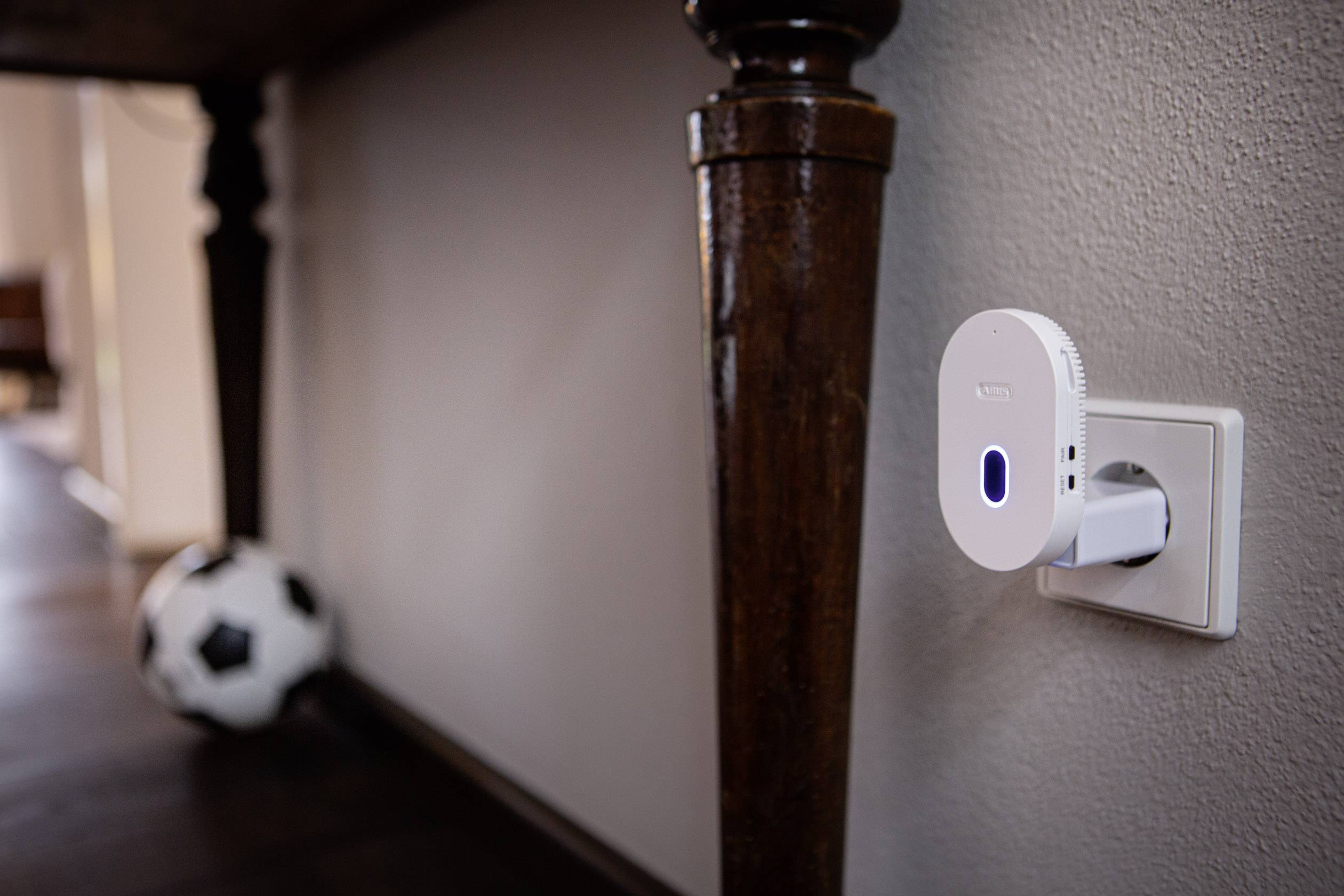 A Wi-Fi repeater is plugged into the wall socket. A blurry football lies on the floor in the background.