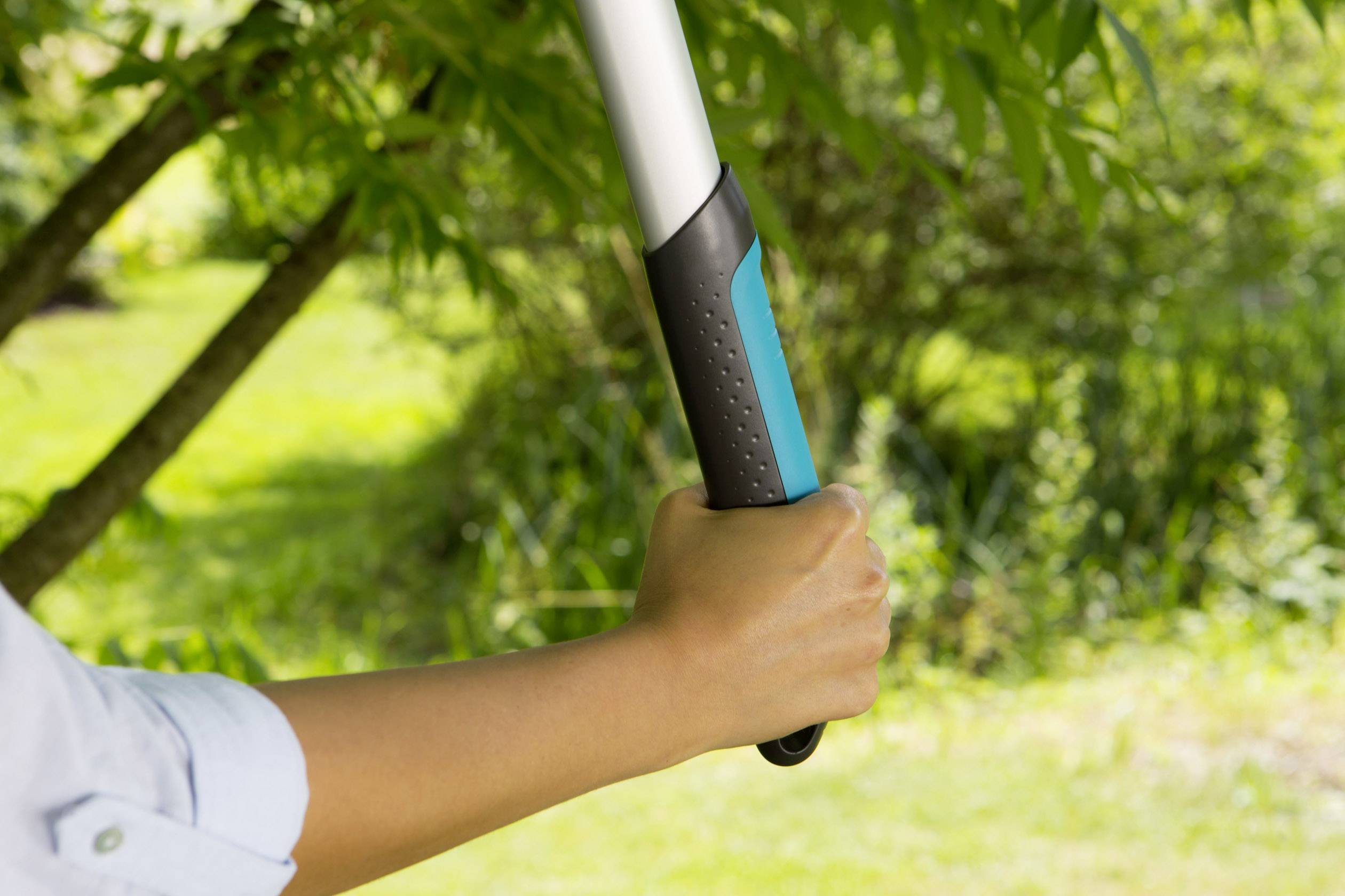 A hand holds a garden tool with a grey handle against a green, overgrown background.