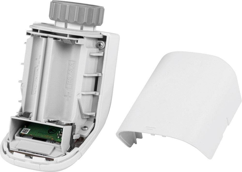 Electronic radiator thermostat without housing cover, showing battery compartment and electronics. The removed cover lies beside it.