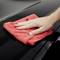 A hand is cleaning the shiny surface of a car with a red cloth.