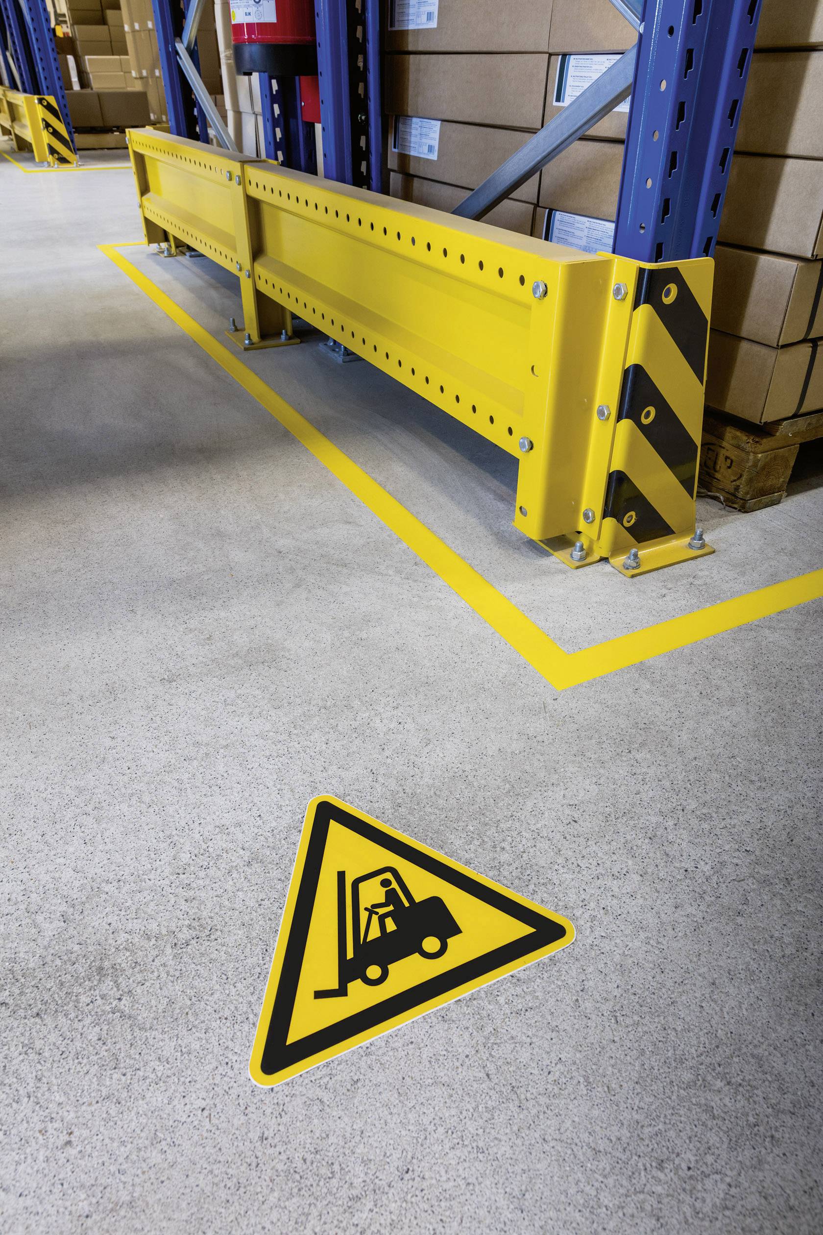 'Warning sign on the floor of a warehouse: Caution Forklift. Yellow barrier and cardboard boxes in the background.'