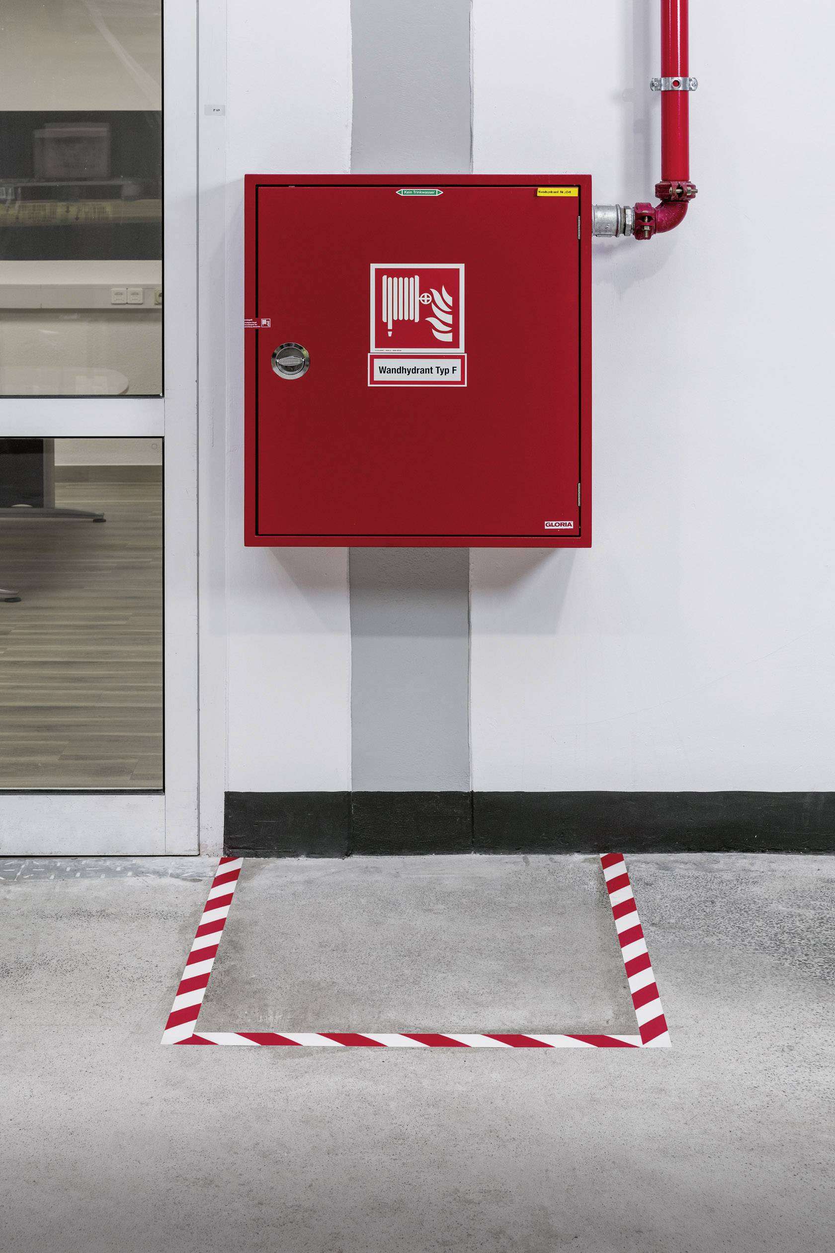 Red fire extinguisher cabinet mounted on a wall, marked with 'Fire Extinguisher Type F' in white lettering. Red metal tube connected at the top.