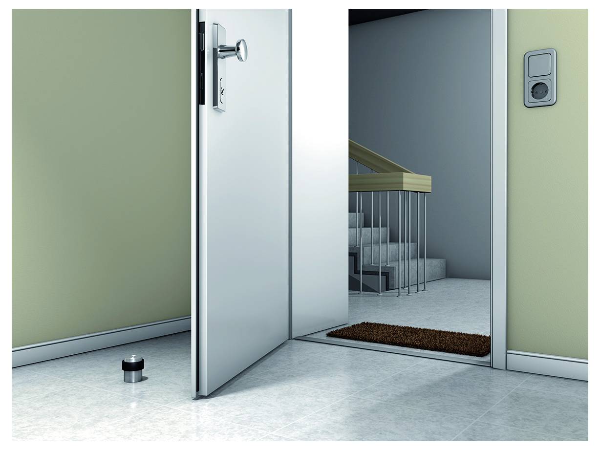 An open door leads to a brightly lit hallway with stairs. A doorstop is placed on the floor. A light switch is on the wall.
