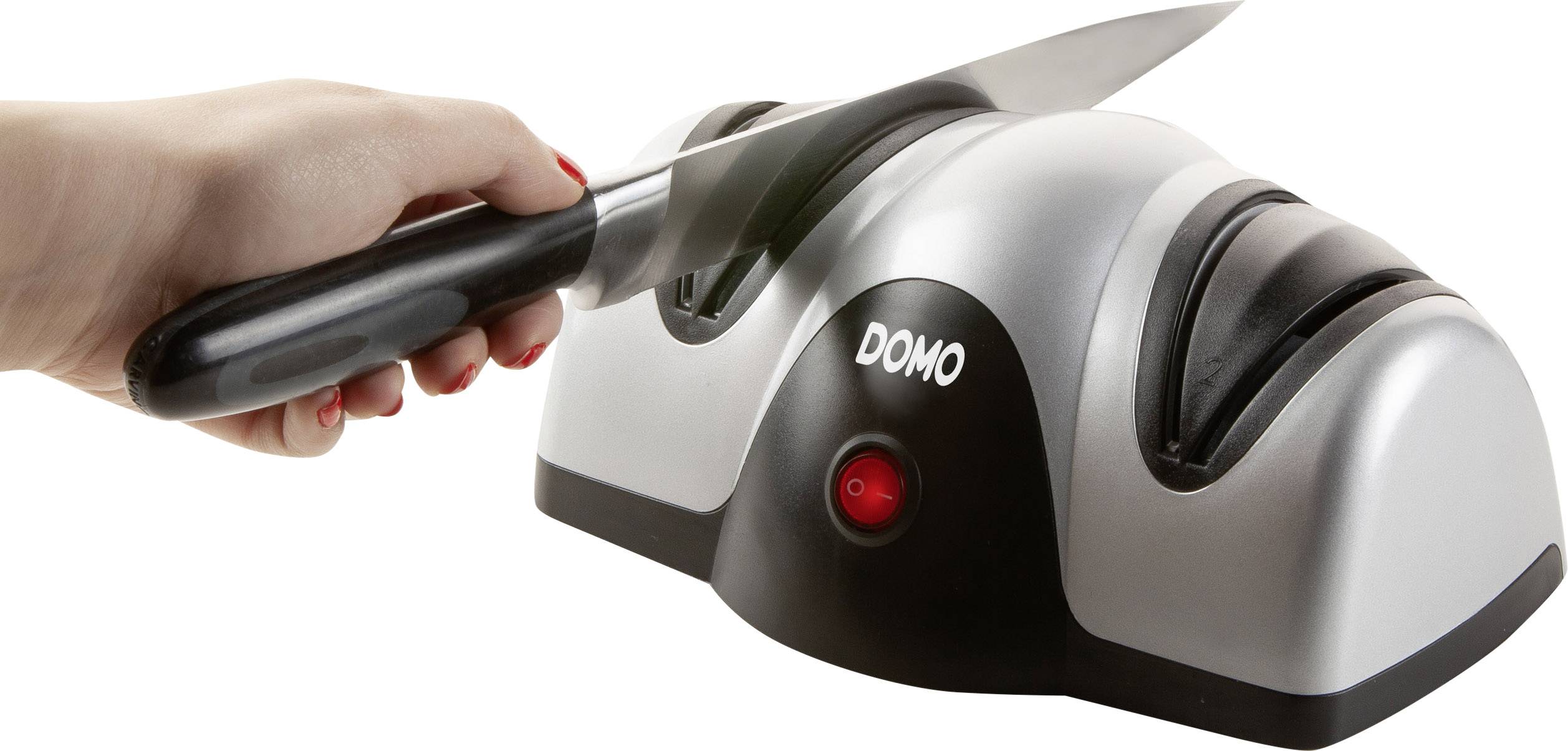 A hand is sharpening a knife with an electric knife sharpener. The device is silver and bears the inscription 'DOMO'.