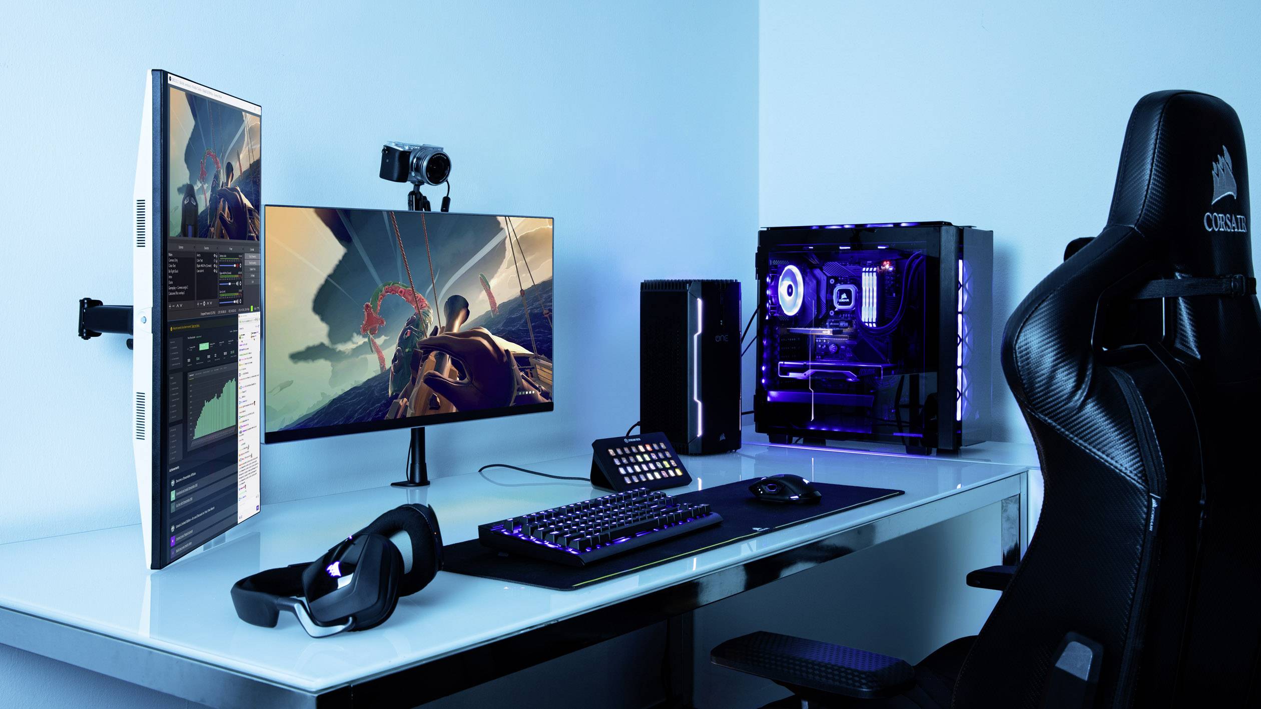 A modern computer workstation with two monitors, a gaming PC, keyboard, mouse, and headset. The room is illuminated with blue light.