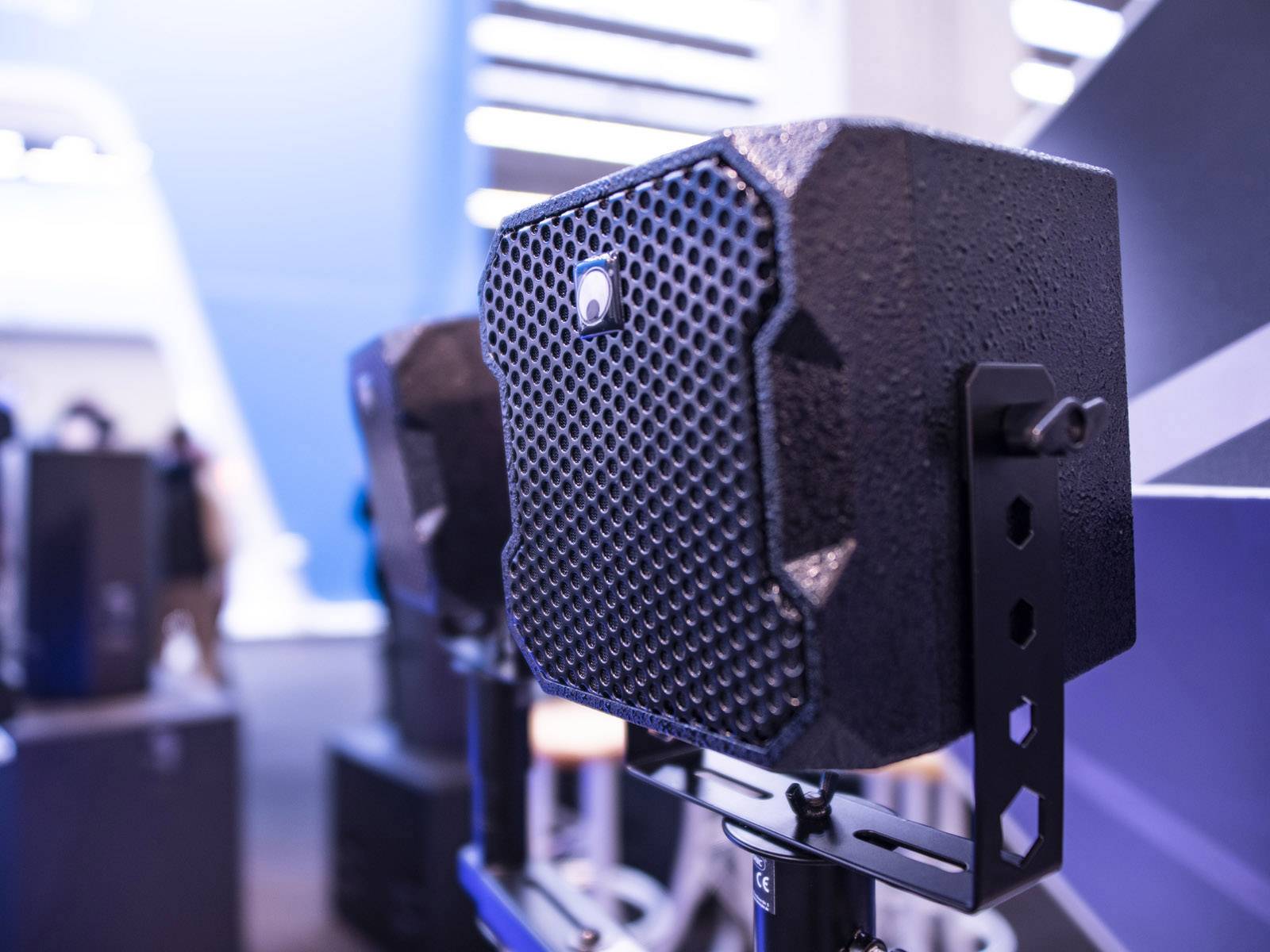 Several speakers are mounted on stands and presented in a modern exhibition space.