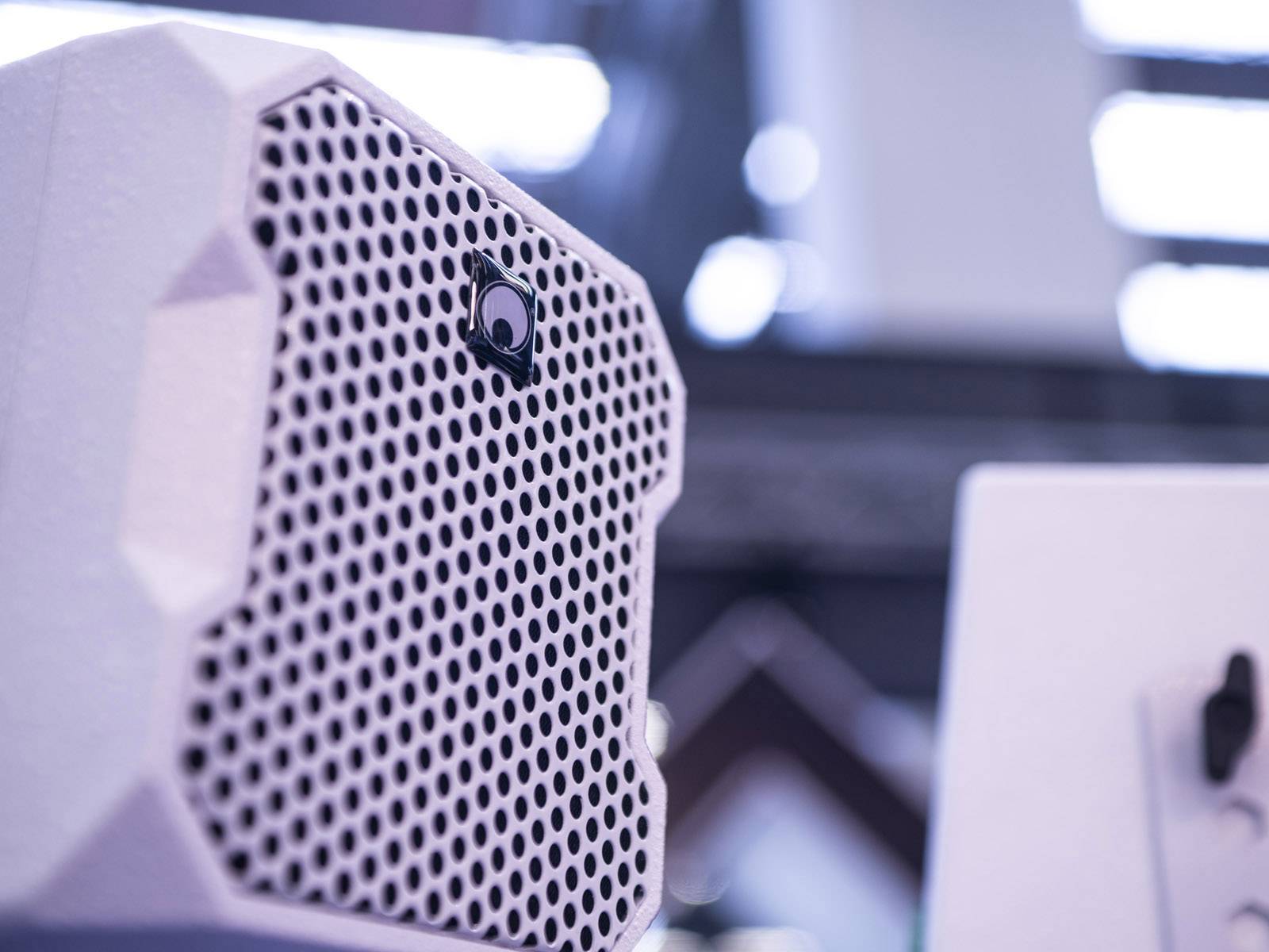 Loudspeaker box with white honeycomb grille design, viewed from the side, in a blurred, modern interior.