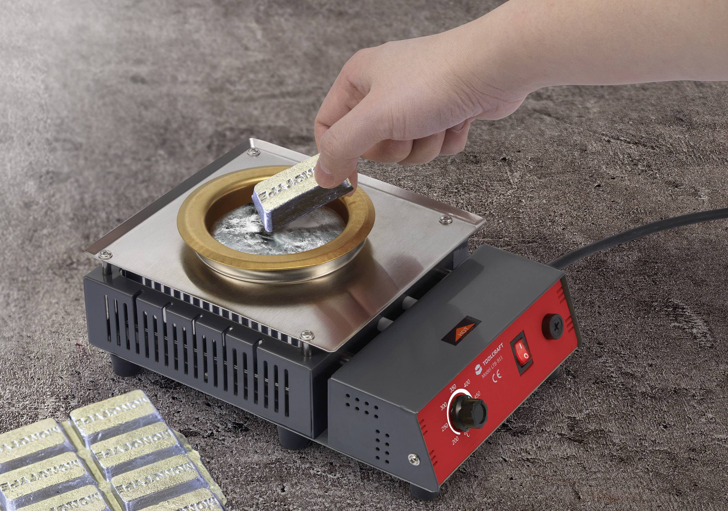 A hand is holding an aluminium part and dipping it into molten lead at a soldering station, likely in preparation for soldering.
