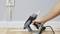 A person is using a hot glue gun to secure a cable trunking strip to a wall above a wooden floor.