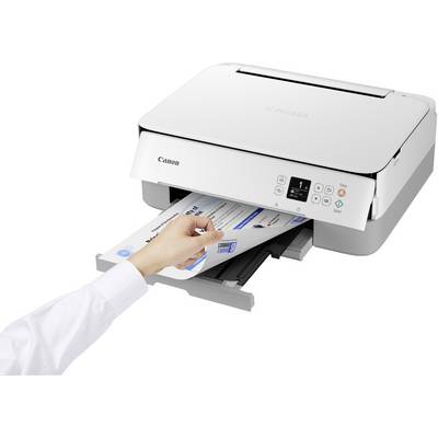 A person removes a printed sheet from a white printer. The printer displays status indicators on a digital display.