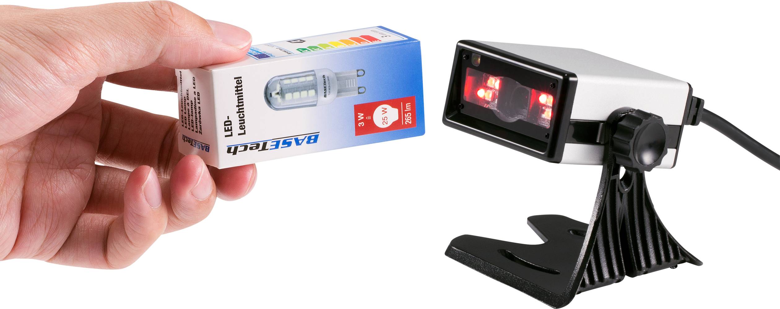 A hand is holding a box containing an LED light bulb. Next to the box, a scanner sits on a stand.