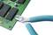 A pair of pliers cuts wires on a green circuit board with multiple electronic components.